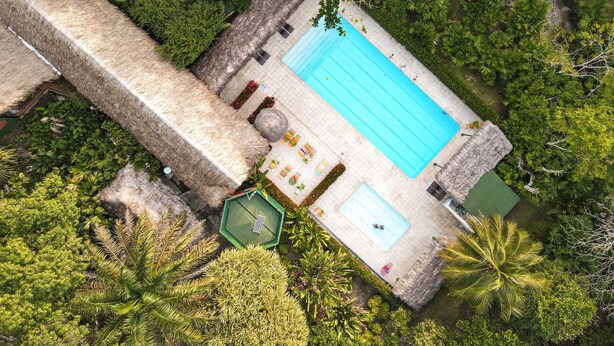 An aerial view of a pool area with a thatched roof, surrounded by lush greenery. - Los Colores Ecoparque (Puerto Triunfo)