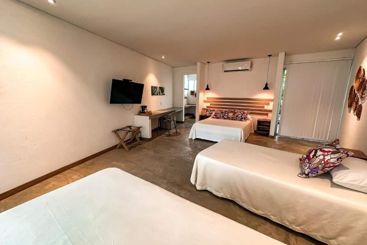 A hotel room with two beds, a desk, a TV, and a dining area.