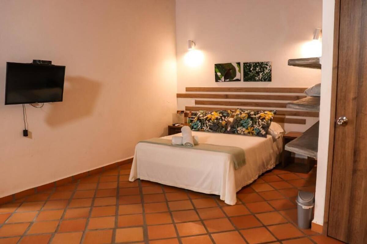A hotel room with a bed, a television mounted on the wall, and a small table with a lamp.