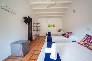 Una habitación de hotel con dos camas, ventilador de techo, televisión y un escritorio pequeño.