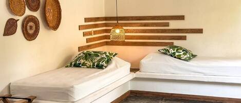 A small, cozy room with two beds, a hanging light fixture, and woven wall decor.