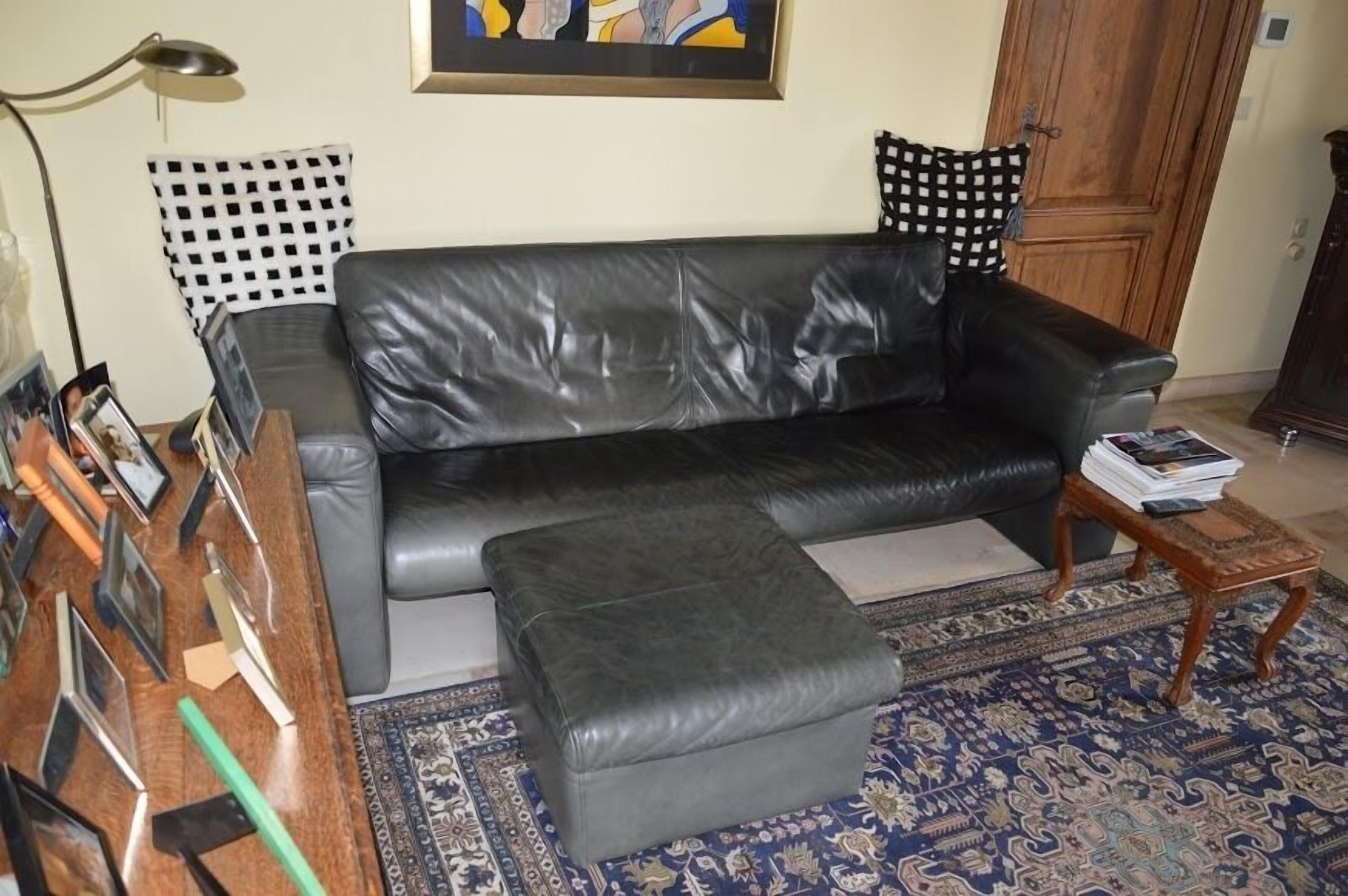 A living room with a black leather sofa, a matching ottoman, a wooden coffee table, a patterned rug, and a framed picture on the wall.