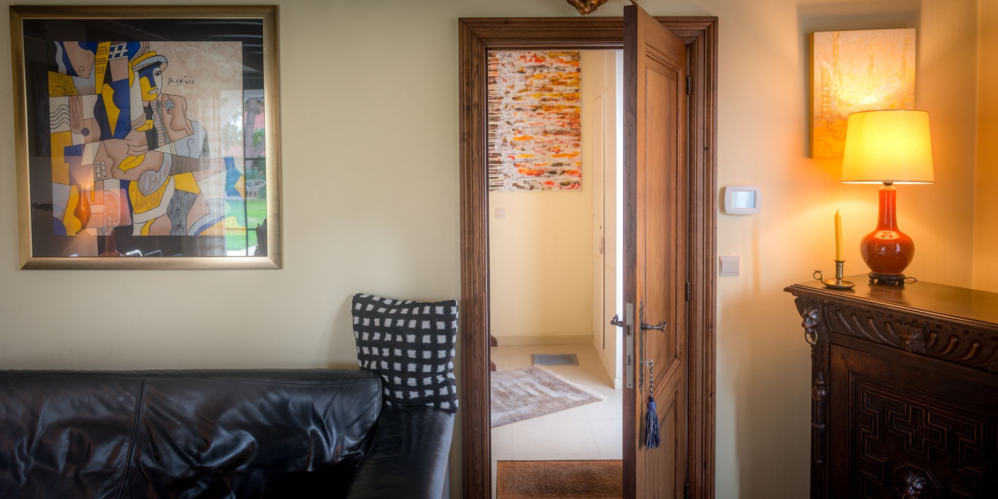 Una habitación con una cama, un sofá de cuero negro, un mueble de madera con una lámpara y un cuadro en la pared.