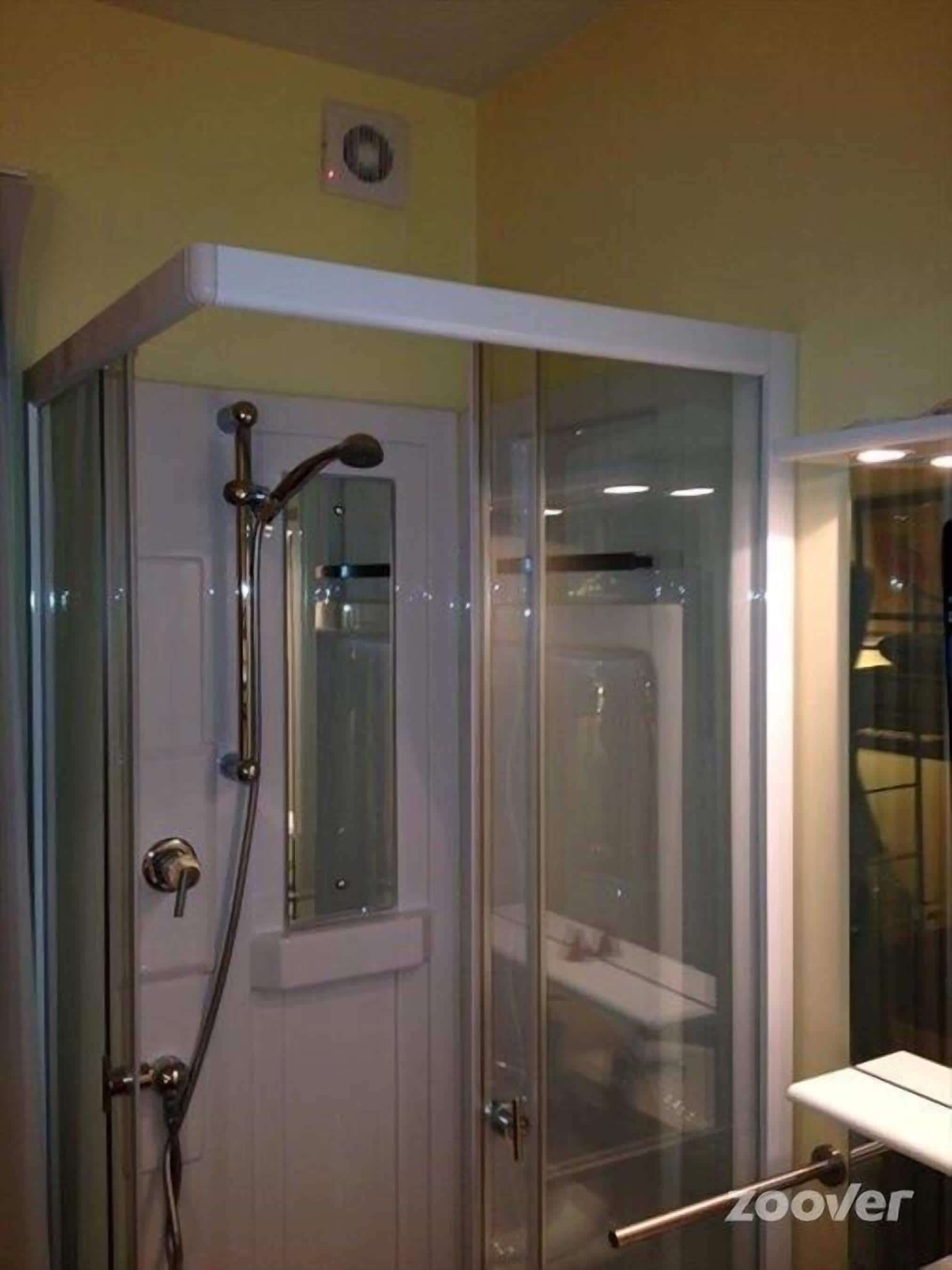 Une cabine de douche fermée par des parois en verre, dotée d’un pommeau de douche à main et d’un robinet fixé au mur.