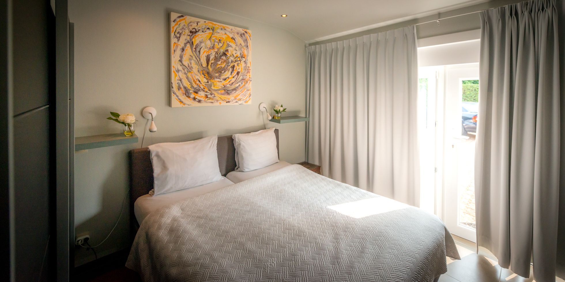 Une chambre d’hôtel avec un lit, un tableau au mur et une fenêtre avec des rideaux.
