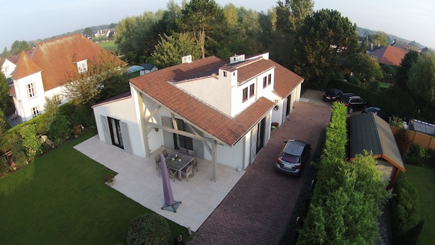 A two-story house with a covered patio, a car parked in the driveway, and a well-maintained garden. - B&B Yaca (De Haan)