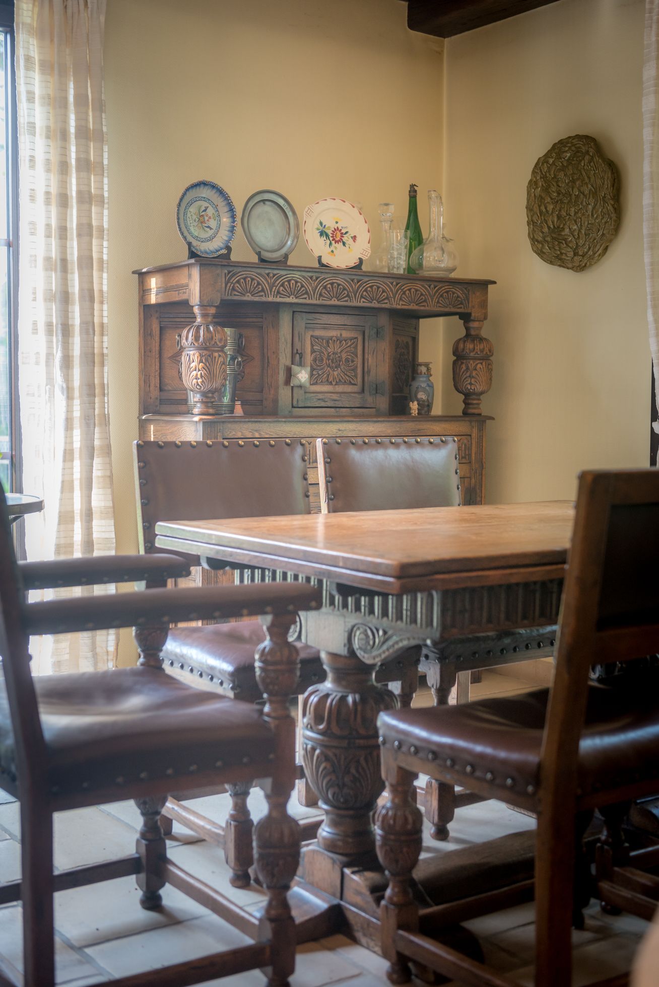 A dining area with a wooden table and chairs, a decorative cabinet with plates, and a textured wall hanging.