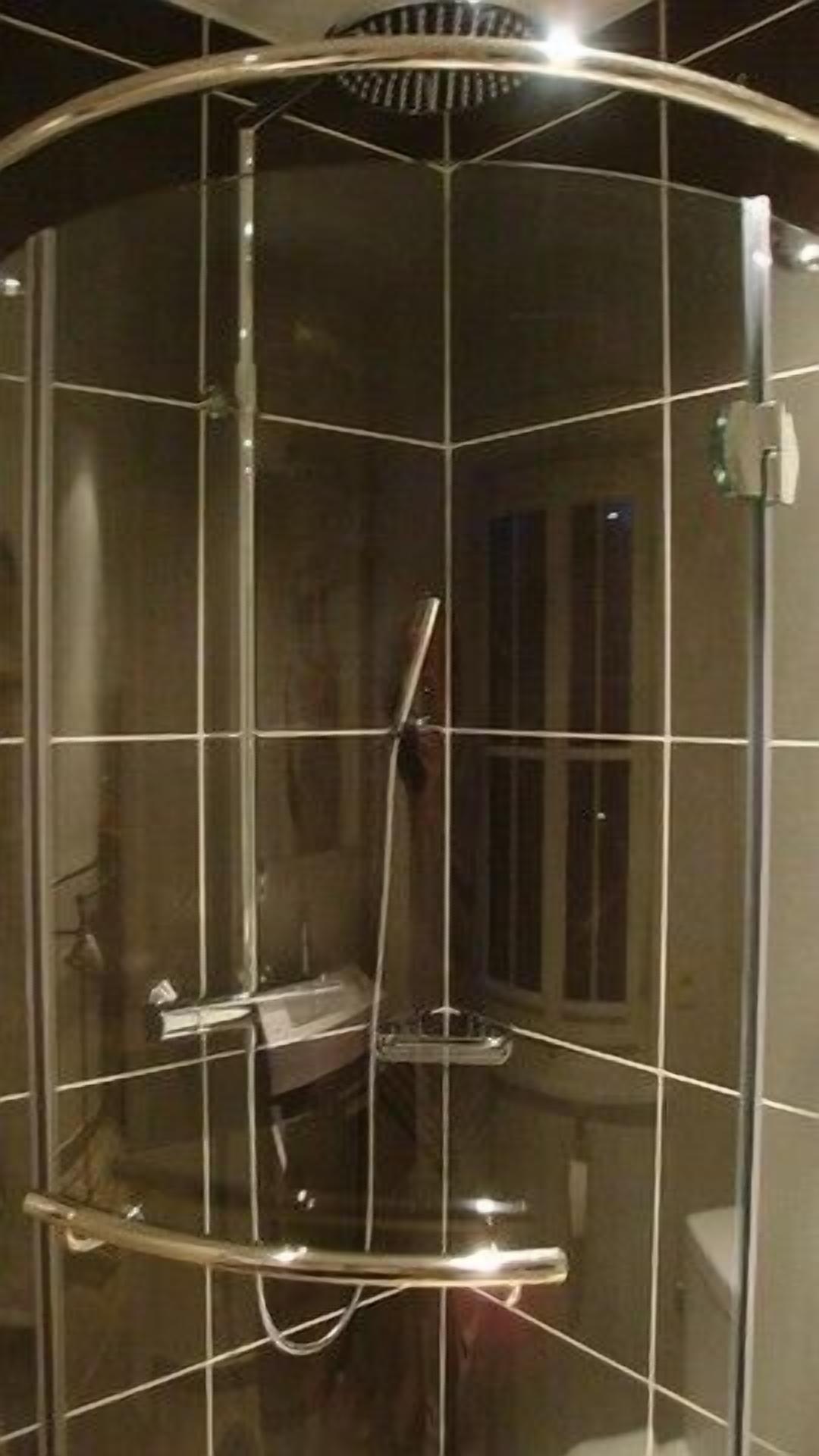 Une cabine de douche fermée par des parois en verre, dotée d’un pommeau de douche à main et d’une petite étagère.
