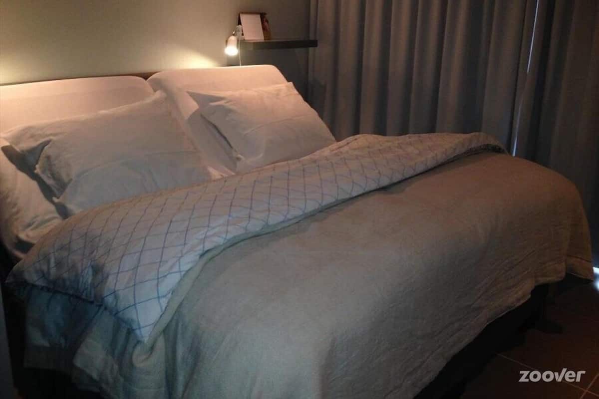 A hotel room with a bed, a nightstand, and a curtain.