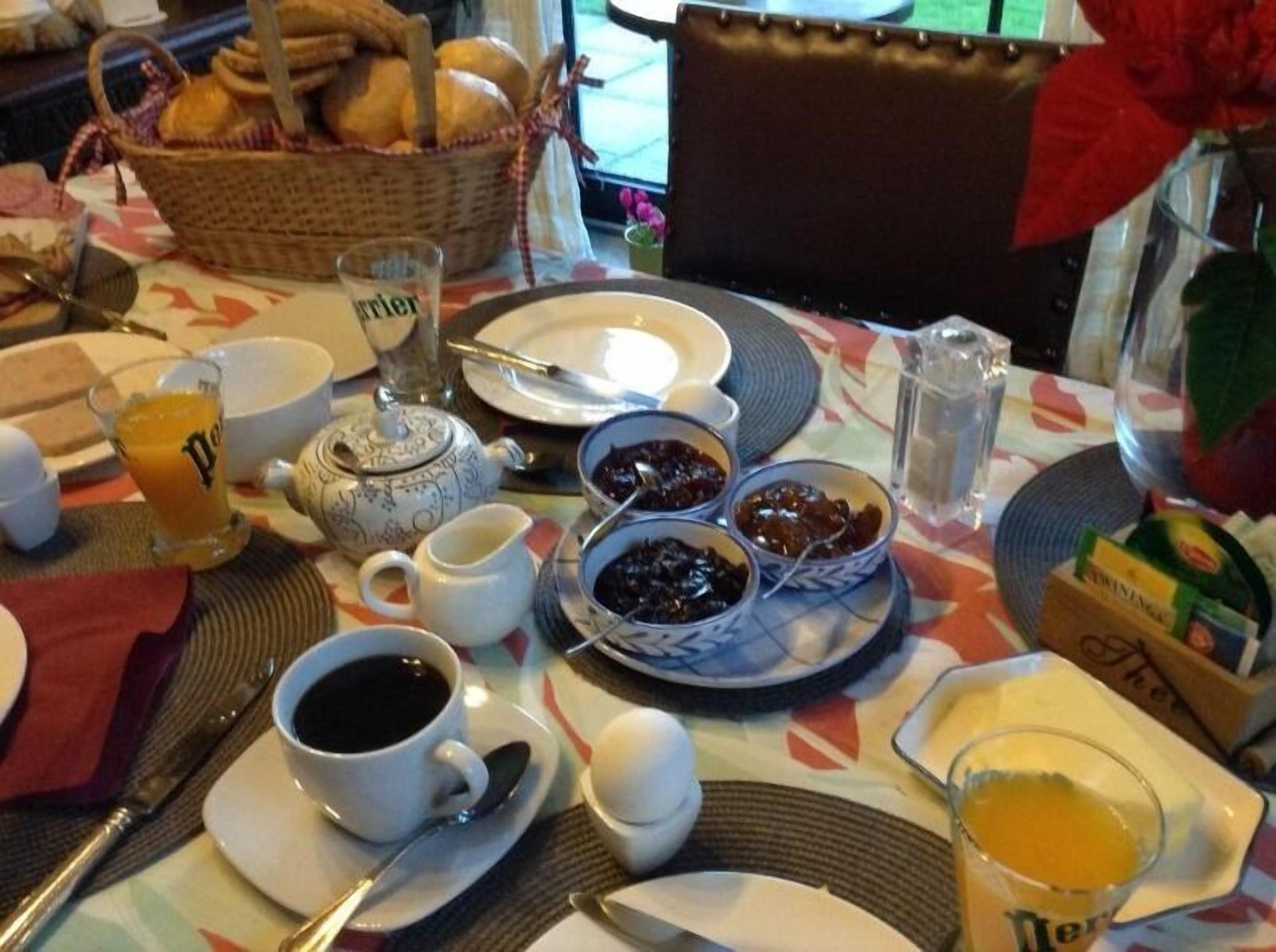 A breakfast table with various dishes, including a teapot, cups, bowls, and a basket of bread.