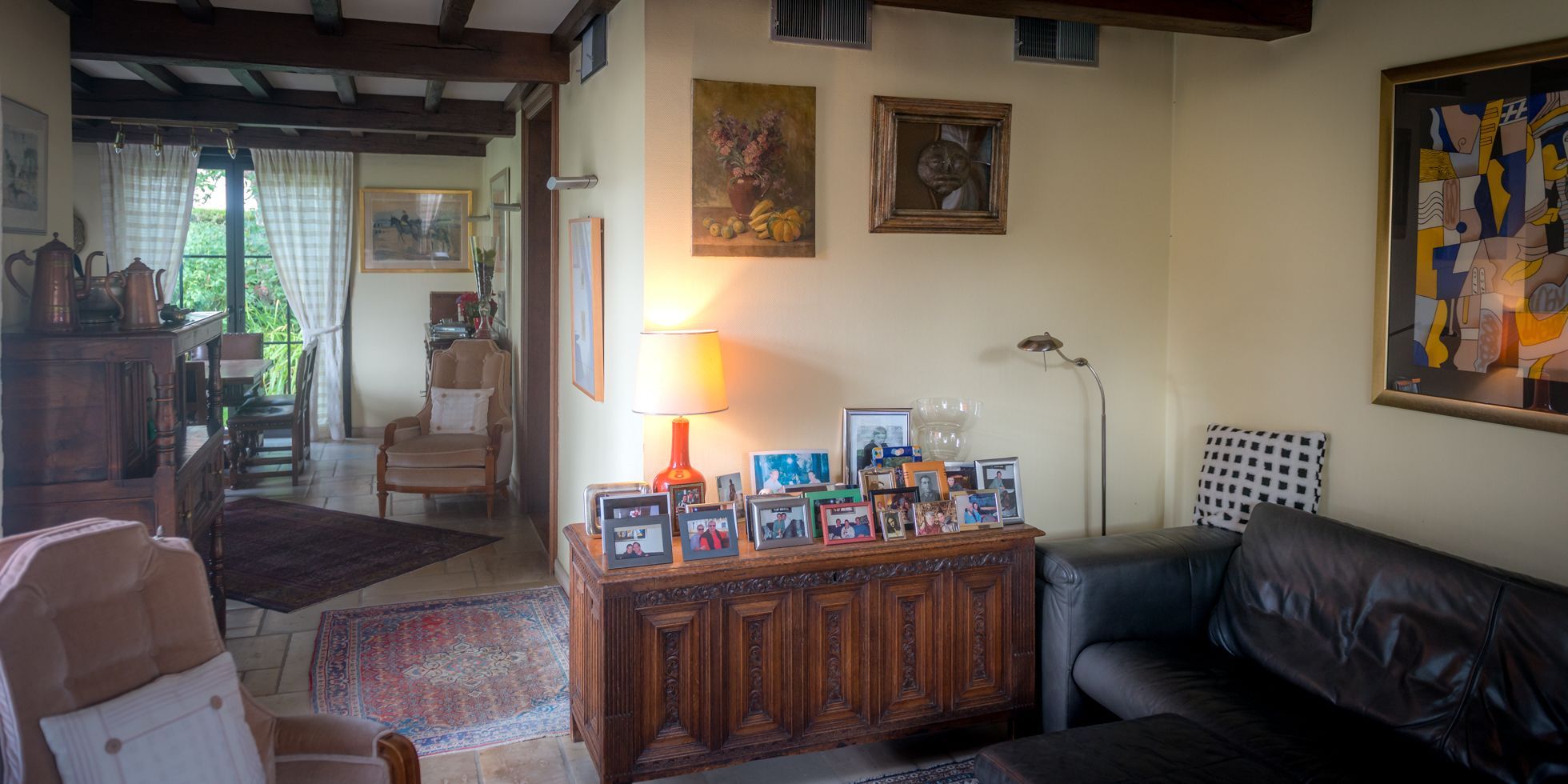 Een gezellige woonkamer met een houten kast met ingelijste foto's, een zwarte leren bank en een kamerbreed tapijt met dessin.