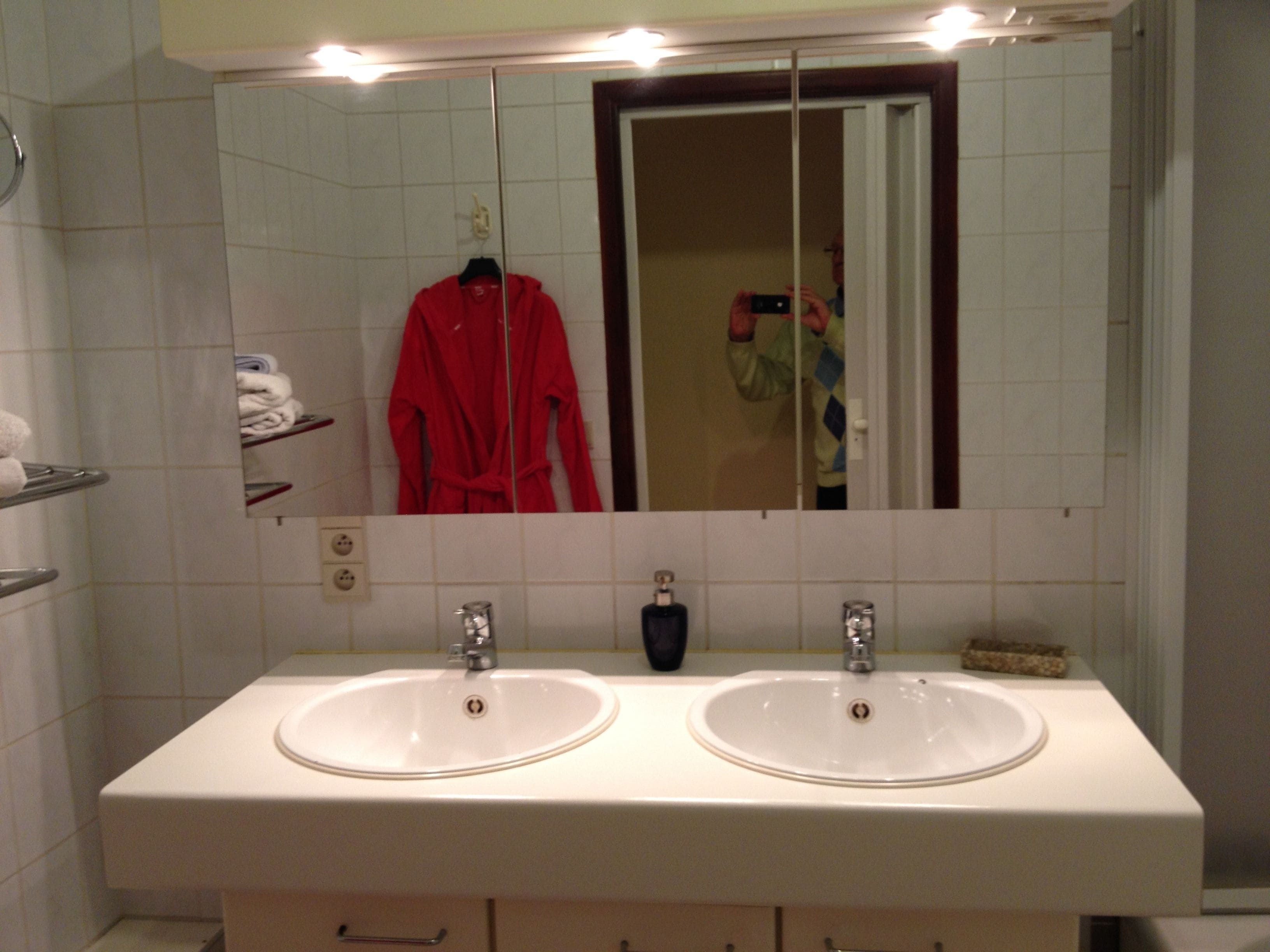 A bathroom with two sinks, a mirror, and a red robe hanging on the wall.
