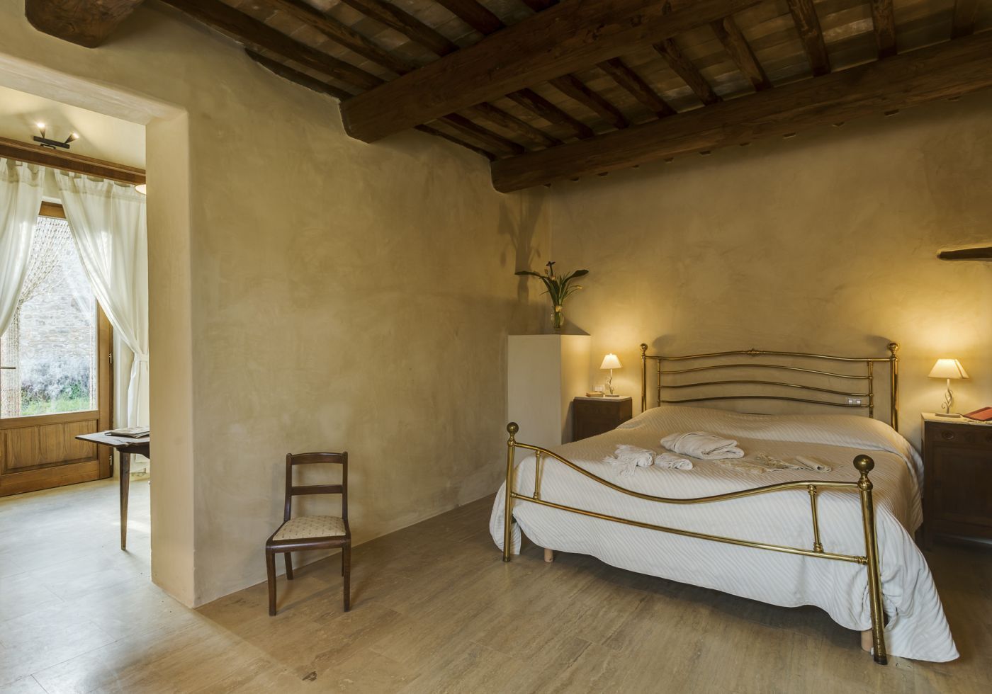 A bedroom with a wooden bed frame, a bedside table with a lamp, a chair, and a window with curtains.
