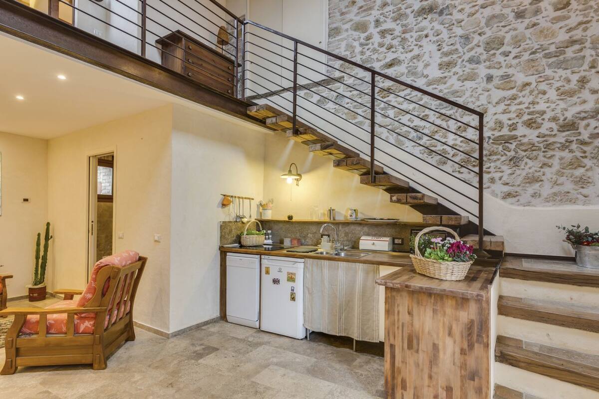 A kitchen with a stone wall, a wooden bench, and a staircase.