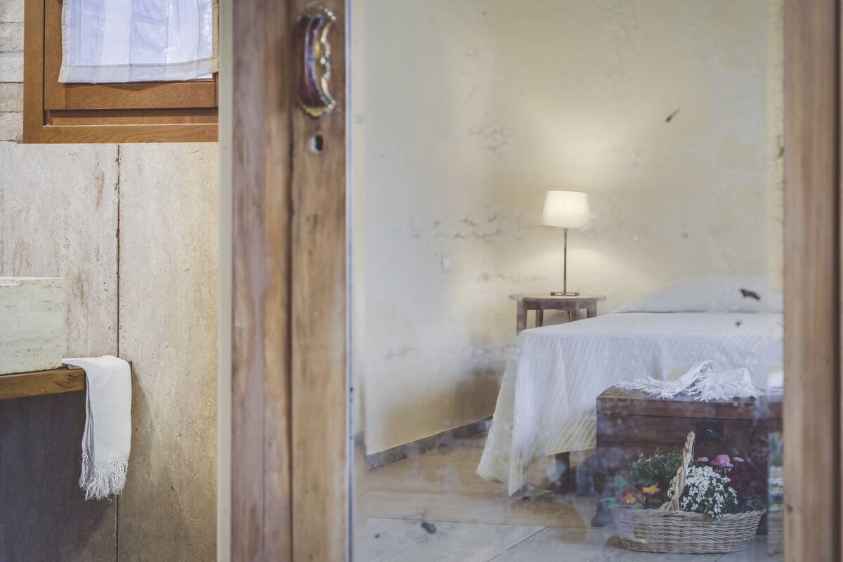A rustic room with a bed, a small table with a lamp, and a basket of flowers.