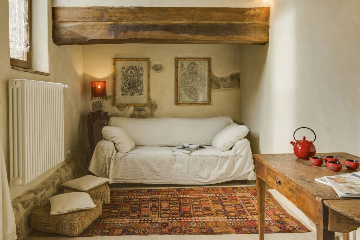 A cozy room with a white sofa, a patterned rug, a red teapot, and a wooden table.