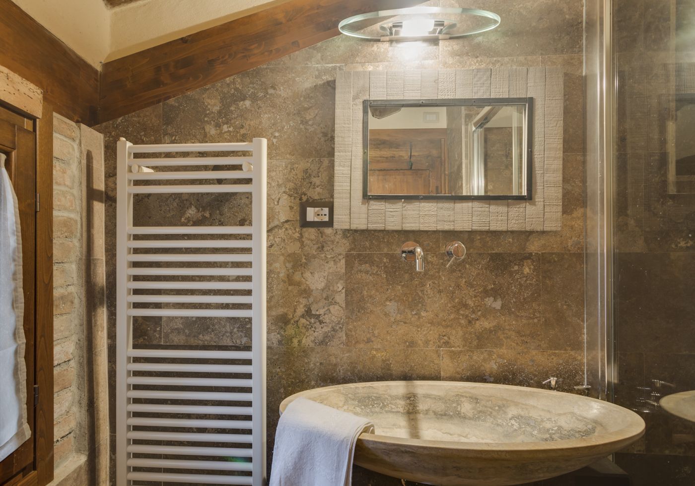 A bathroom with a freestanding bathtub, a towel rack, a mirror, and a stone wall.