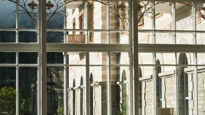 Une grande fenêtre à carreaux multiples, qui reflète un bâtiment à l’architecture en pierre, doté de fenêtres en arc de cercle.