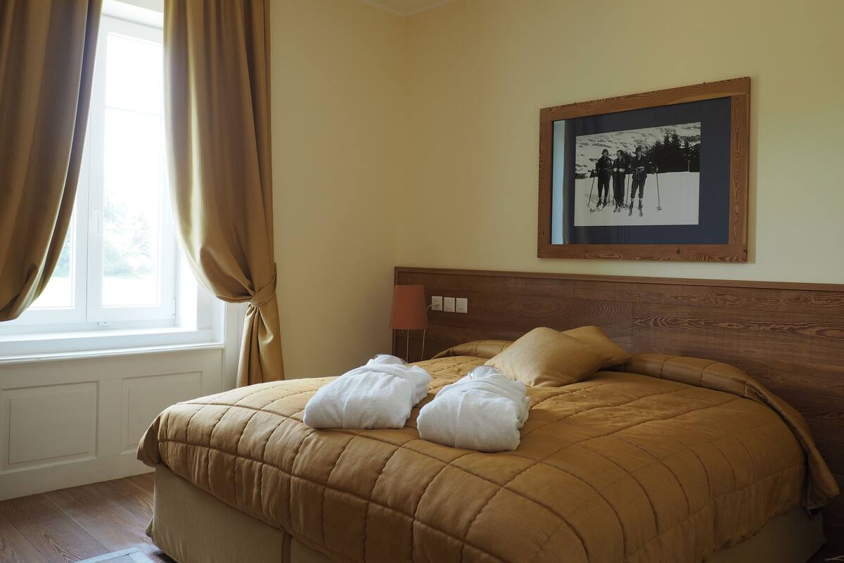 Ein Hotelzimmer mit einem großen Bett, beigen Vorhängen, einem gerahmten Bild an der Wand und einem Fenster mit Vorhängen.