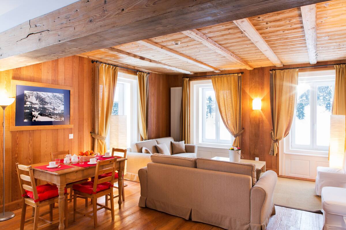 Ein gemütliches Wohnzimmer mit Holzbalken, einer Couch, einem Esstisch mit Stühlen und einem gerahmten Bild an der Wand.