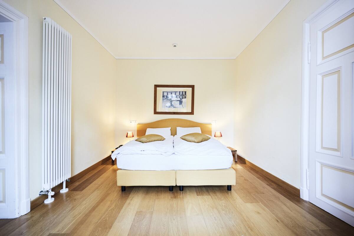 Ein Schlafzimmer mit Doppelbett, Nachttischen, einem gerahmten Bild an der Wand und einer Heizung.