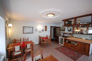 A dining area with a wooden table and chairs, a red tablecloth, and a kitchen with a wooden counter and shelves. - Pension Na Kovárně (Cesky Krumlov)