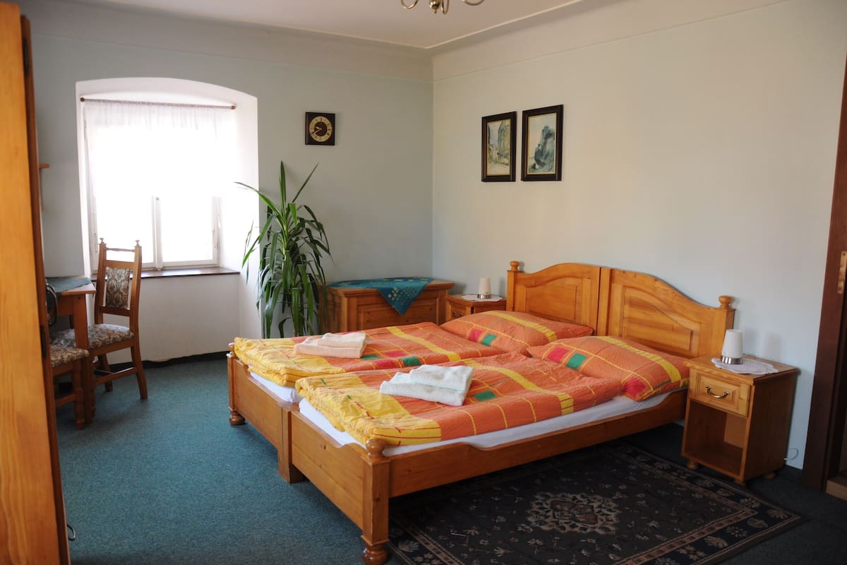 Un dormitorio con cama de madera, una mesita de noche, una silla, una ventana con cortinas y un reloj de pared.