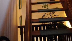 Una escalera de madera con barandilla, un cuadro colgado en la pared y una planta en maceta.