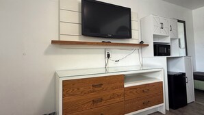 Una kitchenette con una televisión de pantalla plana, armarios de madera, un microondas y un refrigerador.