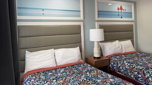 Una habitación de hotel con dos camas, una mesita de noche con una lámpara y dos cuadros en la pared.