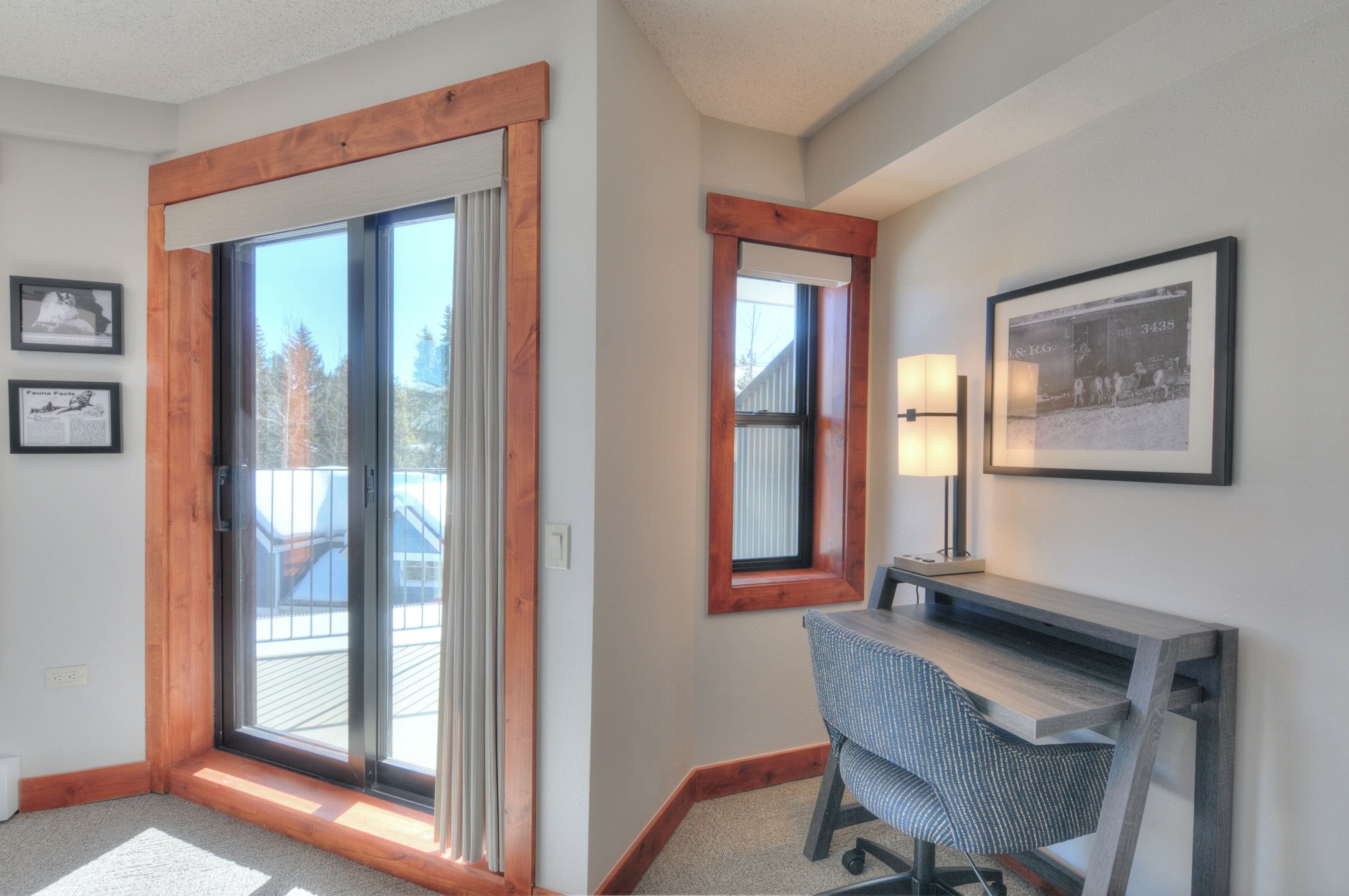 Una stanza con una porta scorrevole in vetro, una scrivania con una sedia, un quadro appeso al muro e una finestra con cornice in legno.