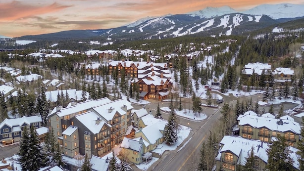 A large lodge with multiple buildings, surrounded by snow-covered trees and mountains in the background. - Wedgewood Lodge (Breckenridge)