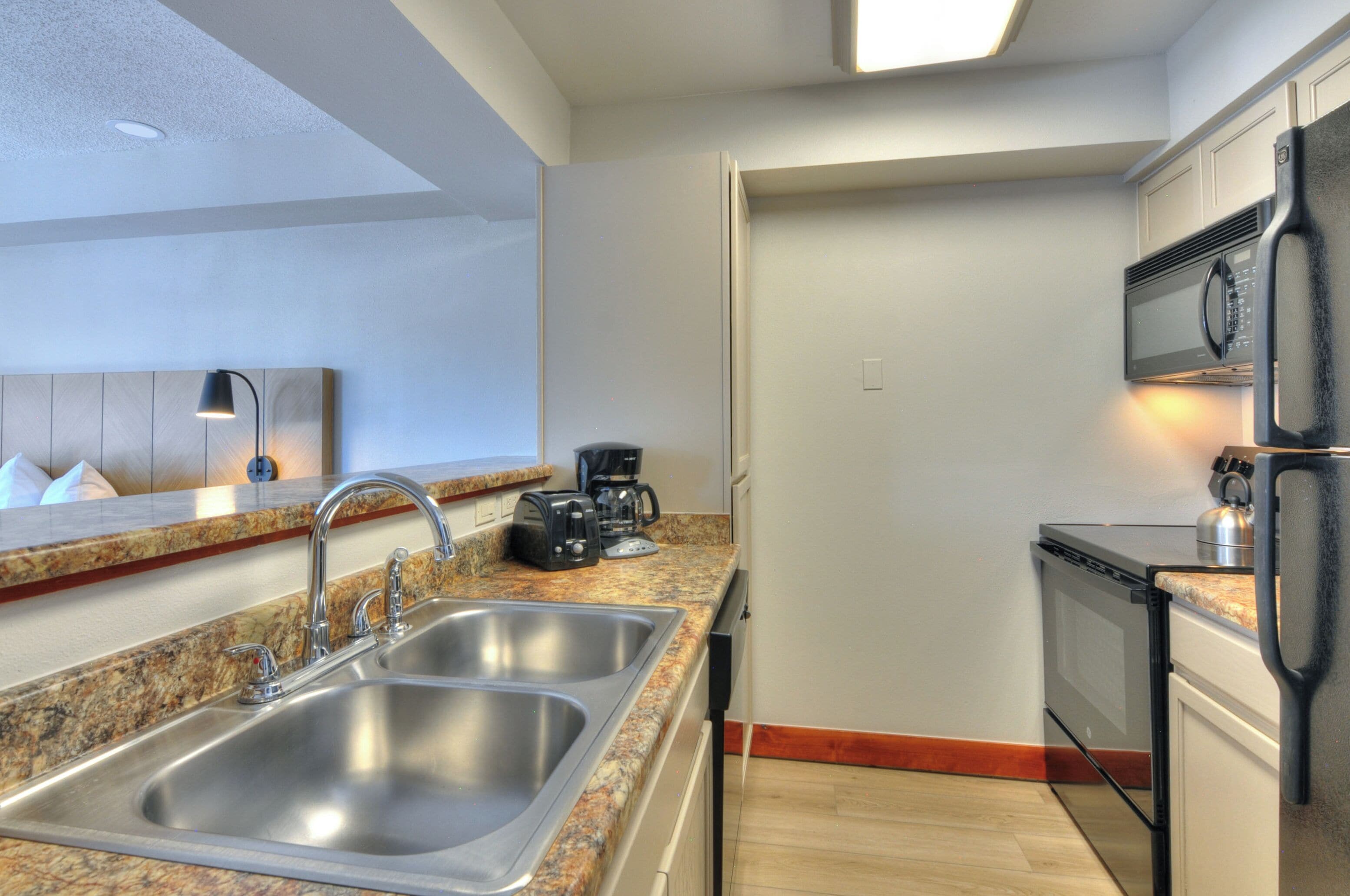 Eine moderne Küche mit Granit Arbeitsplatten, Edelstahl-Spülen, einer eingebauten Mikrowelle und einem schwarzen Kühlschrank.