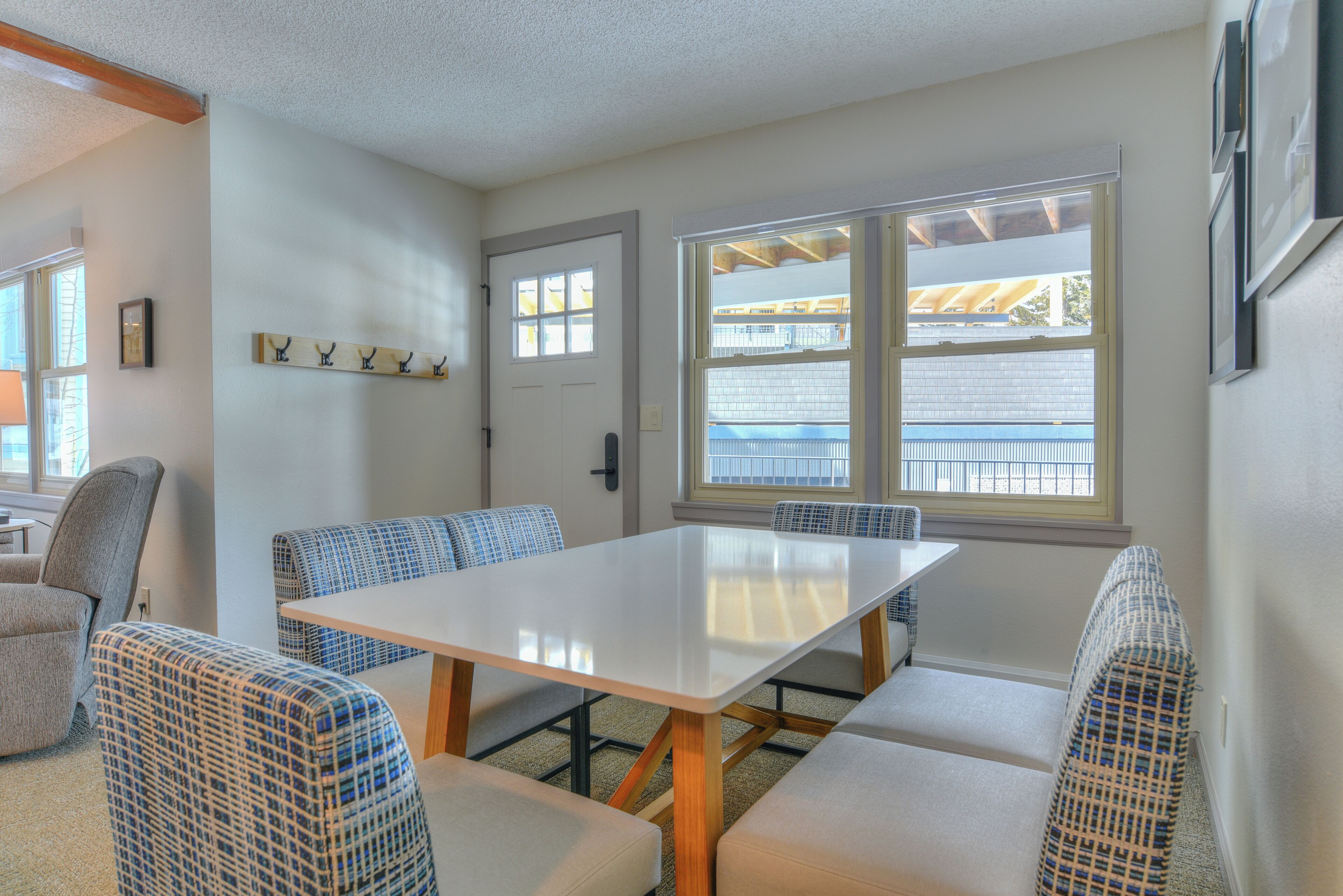 A room with a white table and blue patterned chairs, a door, and windows with a view of a building.