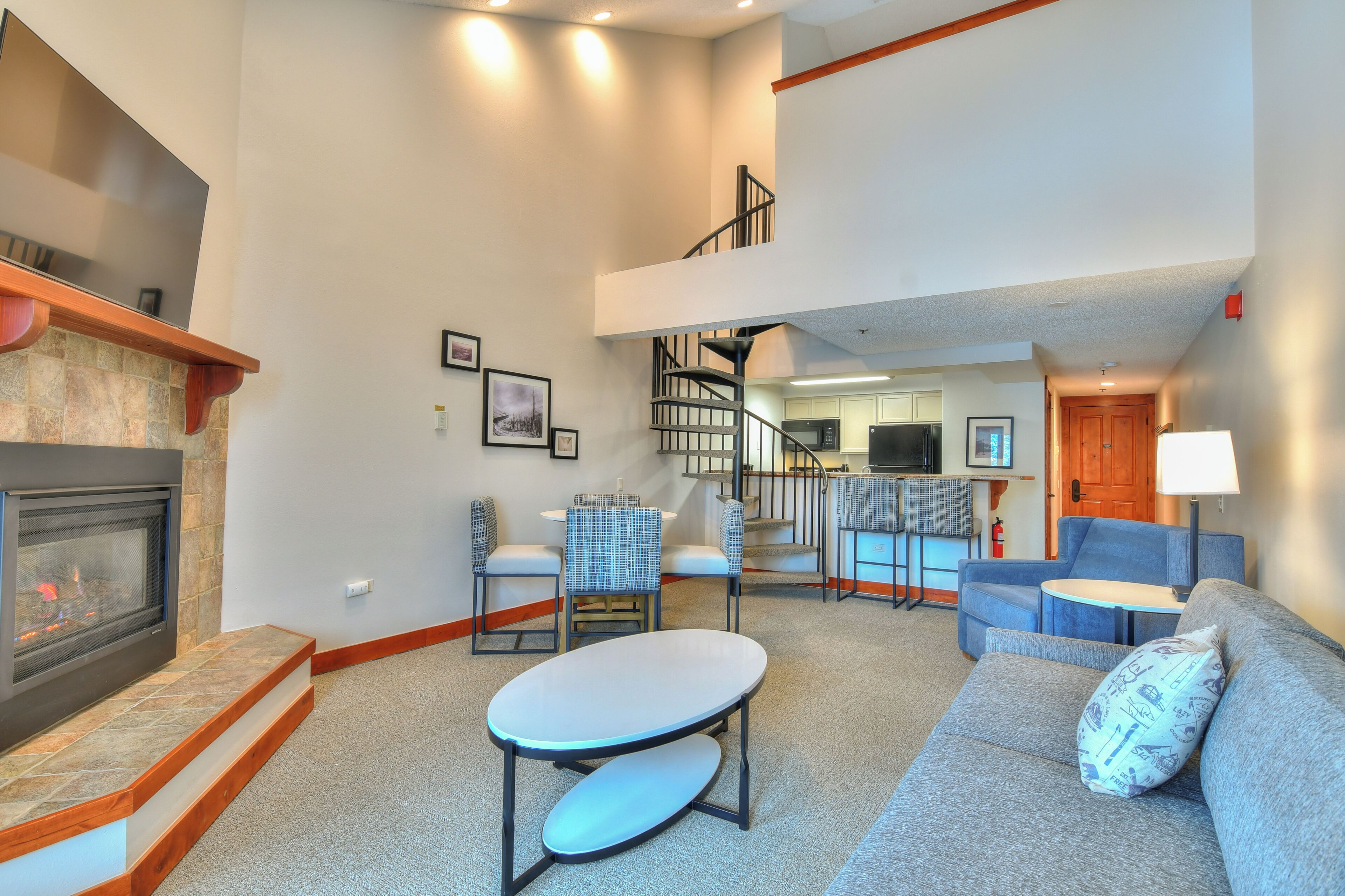A spacious living area with a fireplace, a sofa, a dining table, and a staircase leading to an upper level.