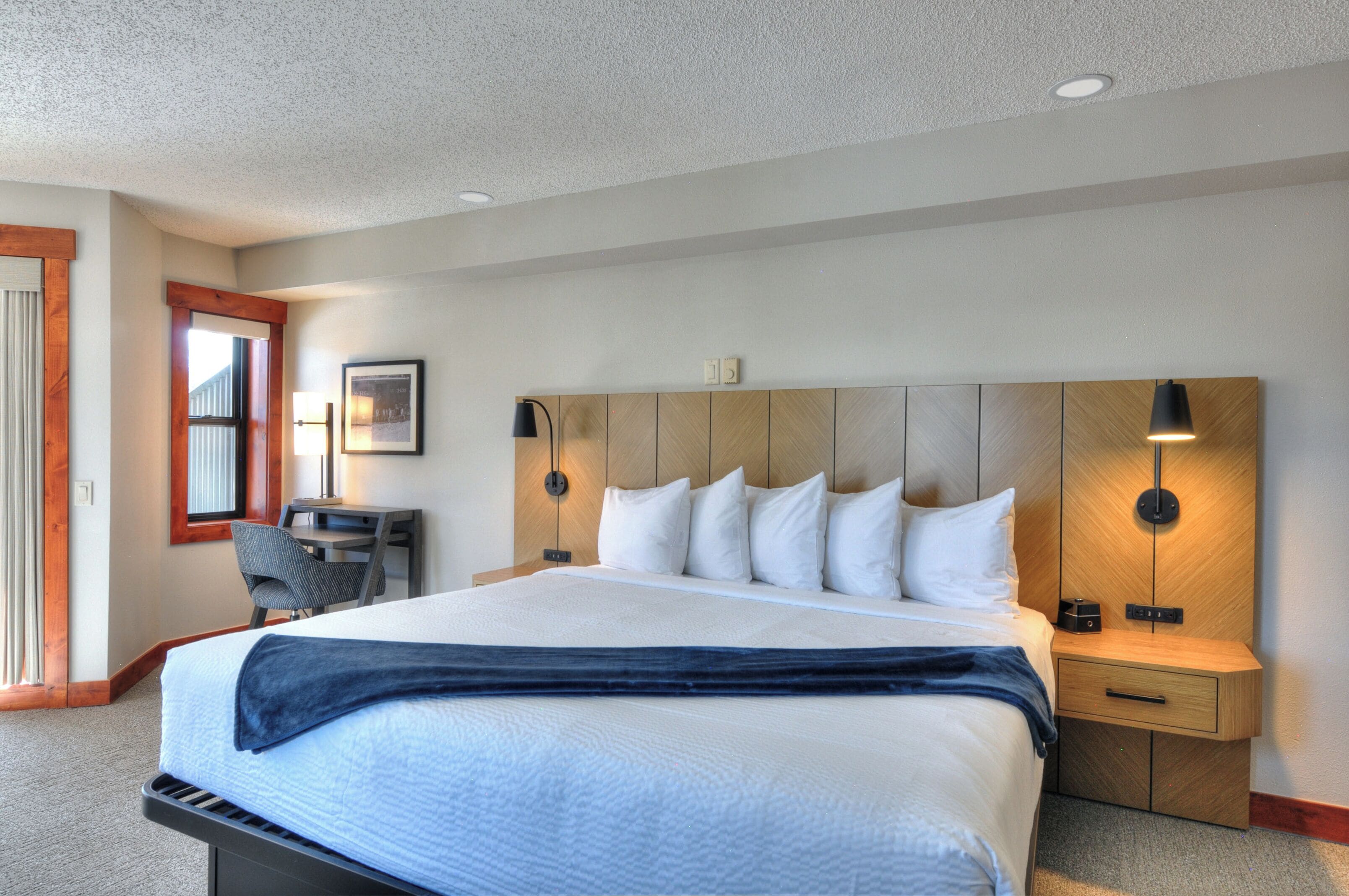 A modern hotel room with a large bed, a desk, and a chair.
