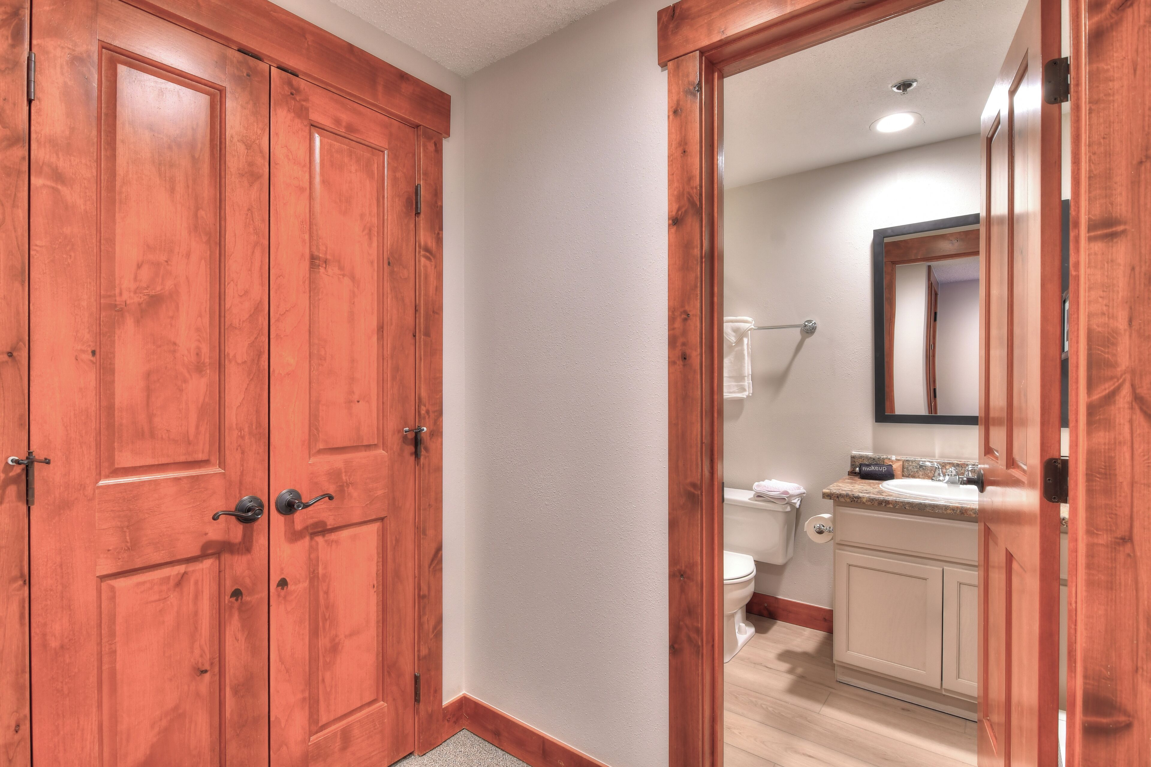 Puerta de madera que da a un baño con inodoro, lavabo y espejo.