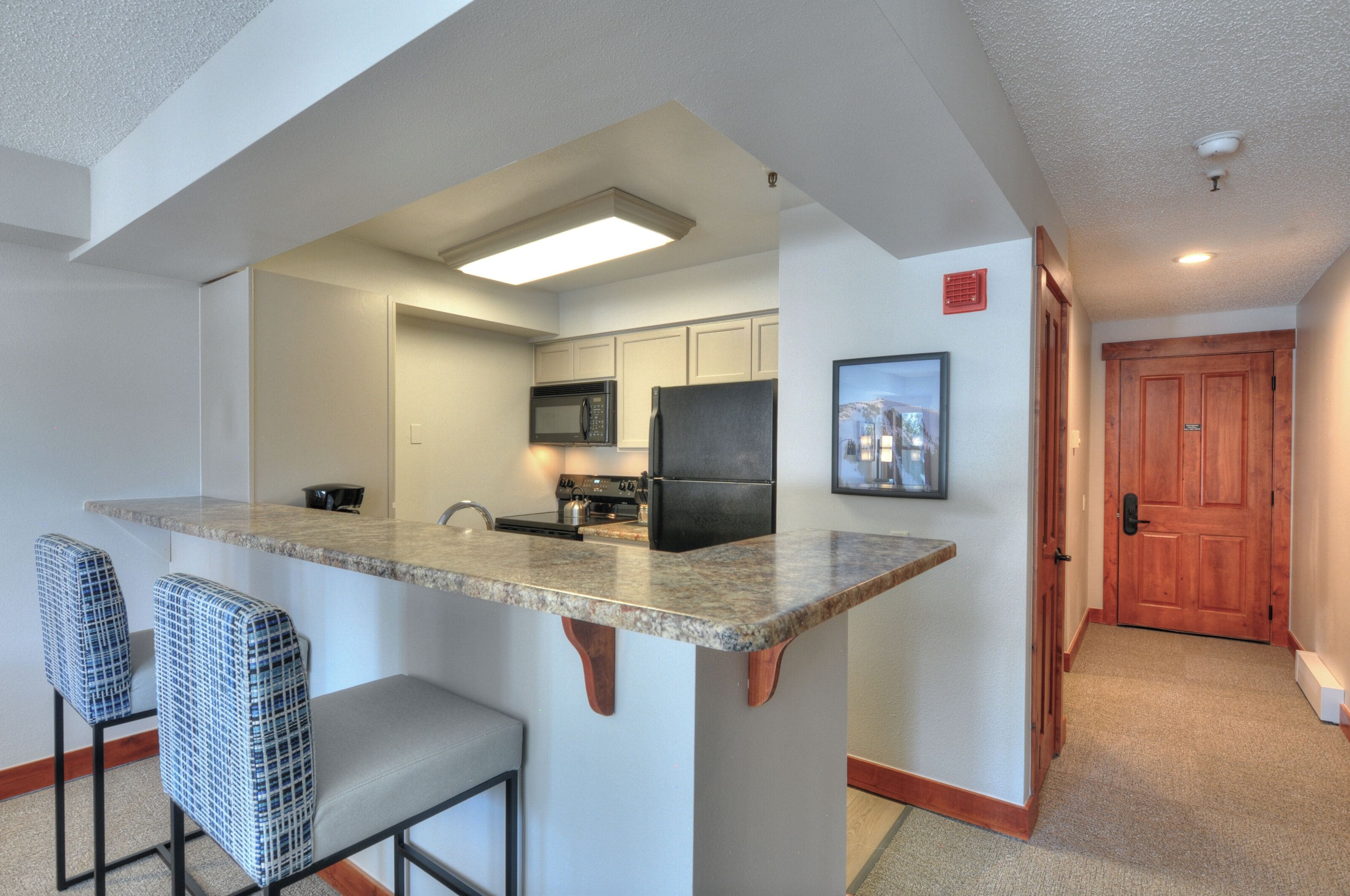 A compact kitchen with a central island, bar stools, and a microwave.