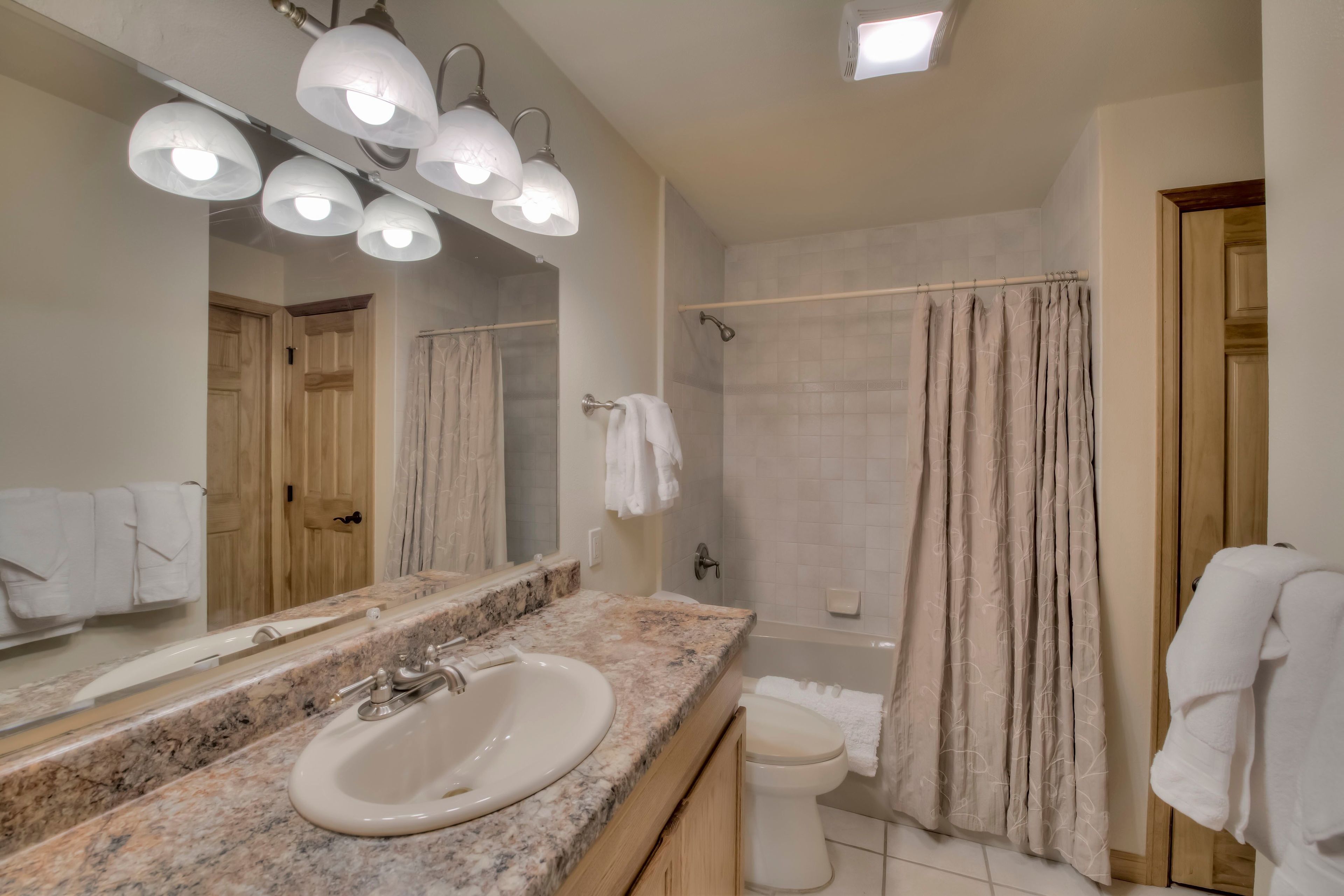 Un baño con lavamanos de encimera de granito, un espejo grande y una ducha con cortina color beige.