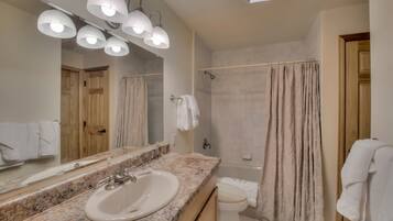 Un baño con lavamanos de encimera de granito, un espejo grande y una ducha con cortina color beige.