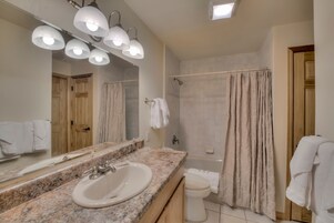 Un baño con lavamanos de encimera de granito, un espejo grande y una ducha con cortina color beige.