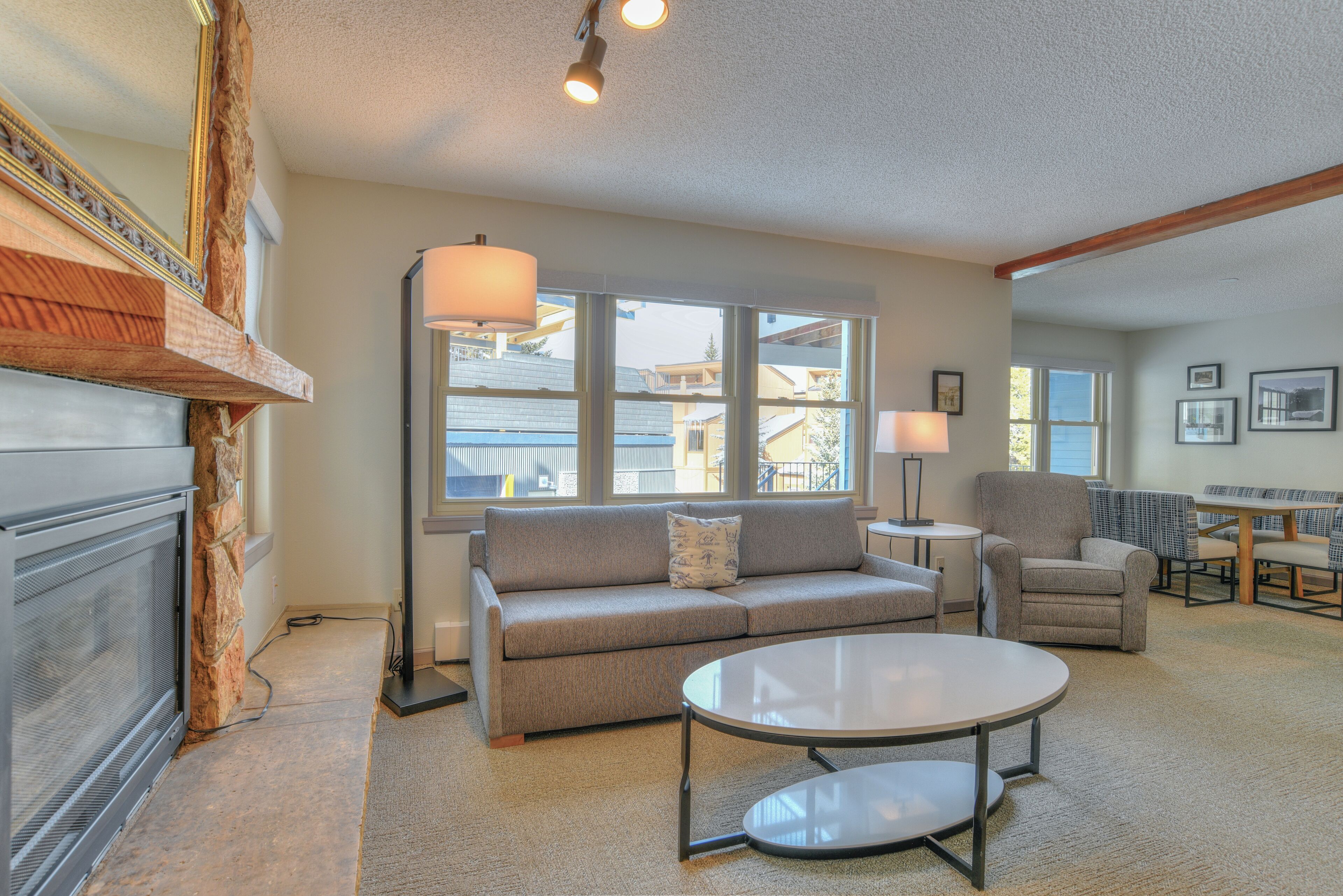 A living room with a fireplace, a sofa, a round coffee table, and a view of the outside.