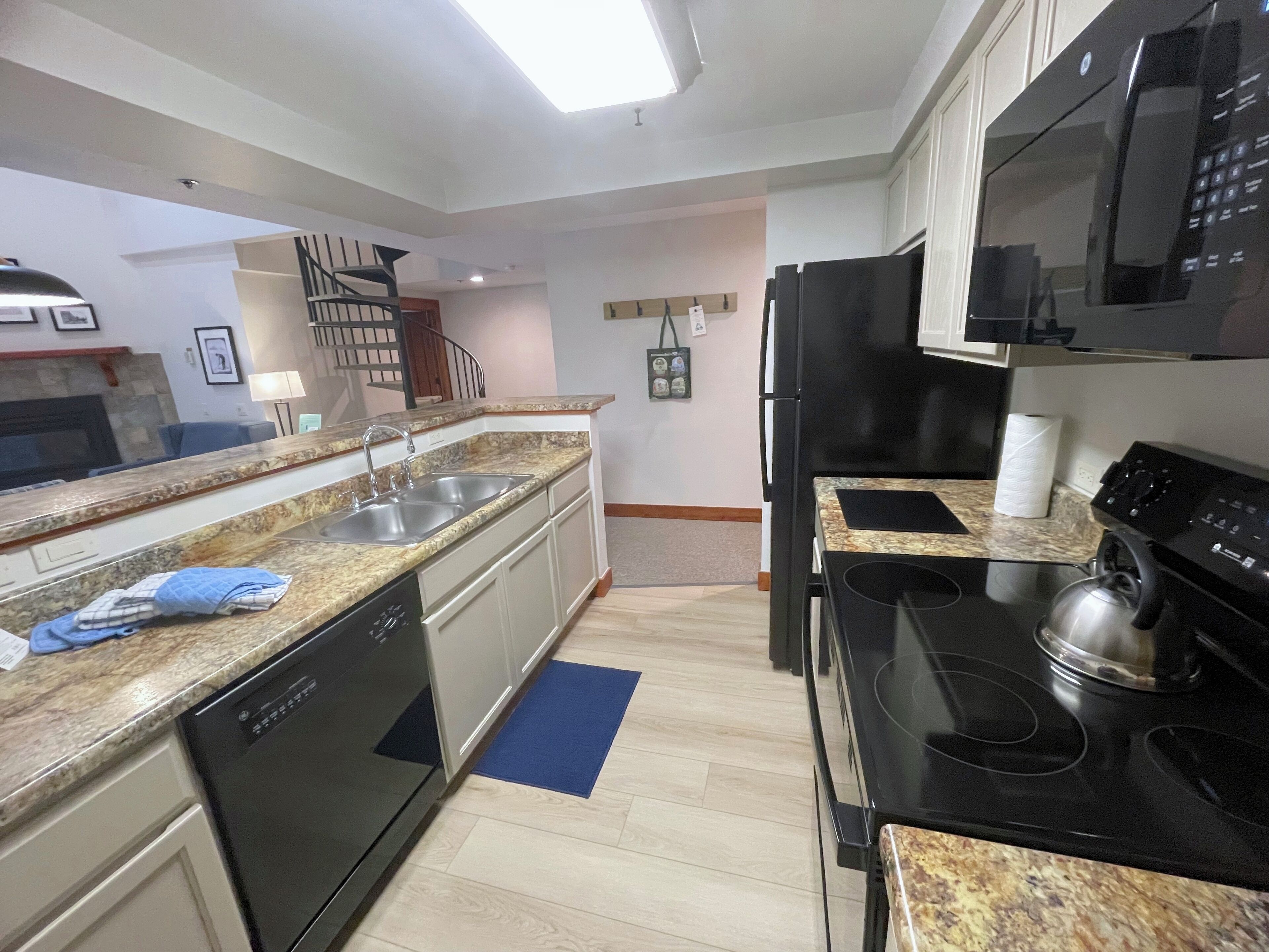 A modern kitchen with granite countertops, stainless steel appliances, and a blue rug on the floor.