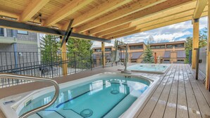 A wooden deck with a pool and hot tubs, surrounded by buildings and trees. - Wedgewood Lodge (Breckenridge)