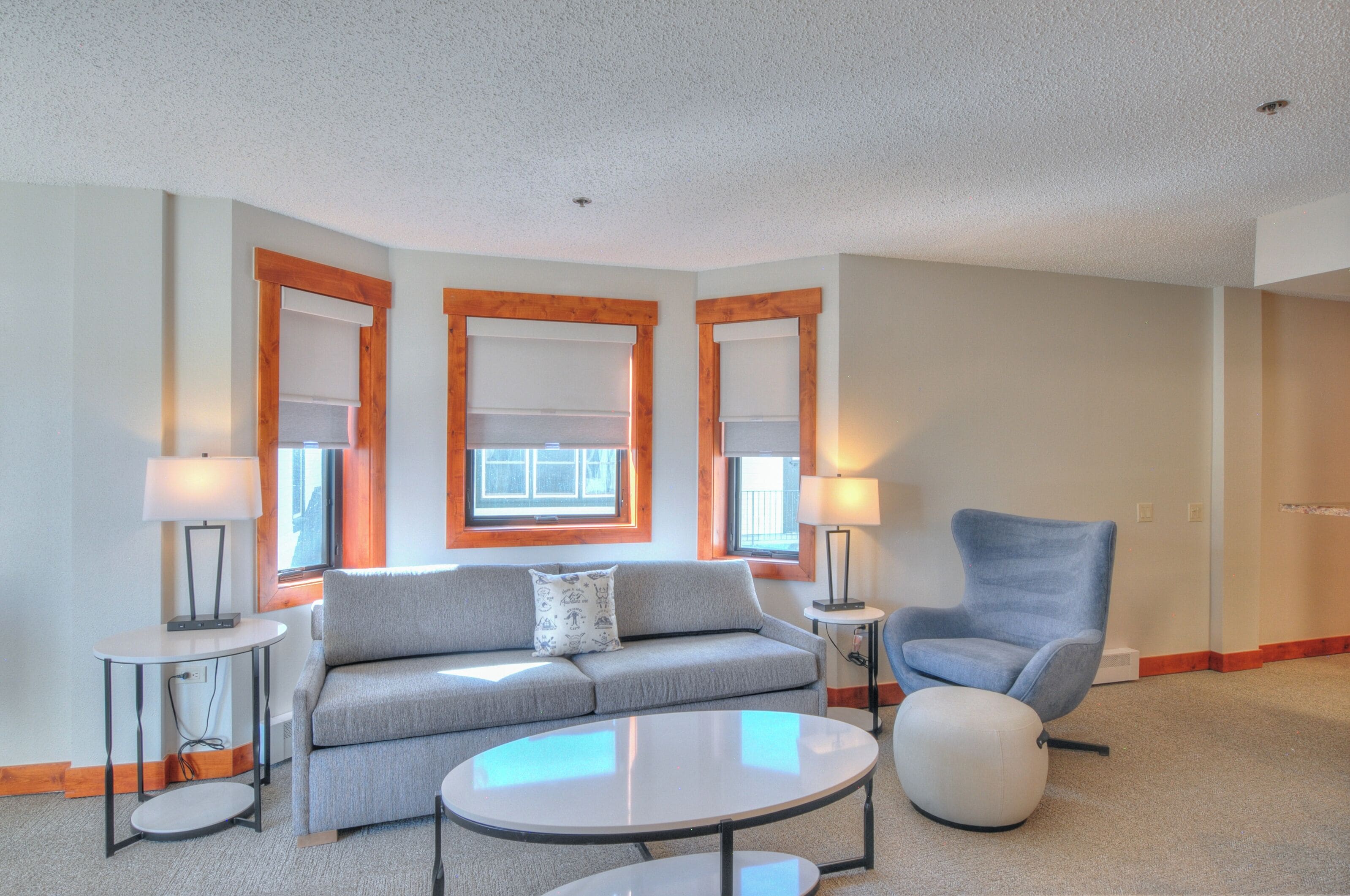 A modern living room with a grey sofa, two side tables with lamps, a blue armchair, and a round coffee table.