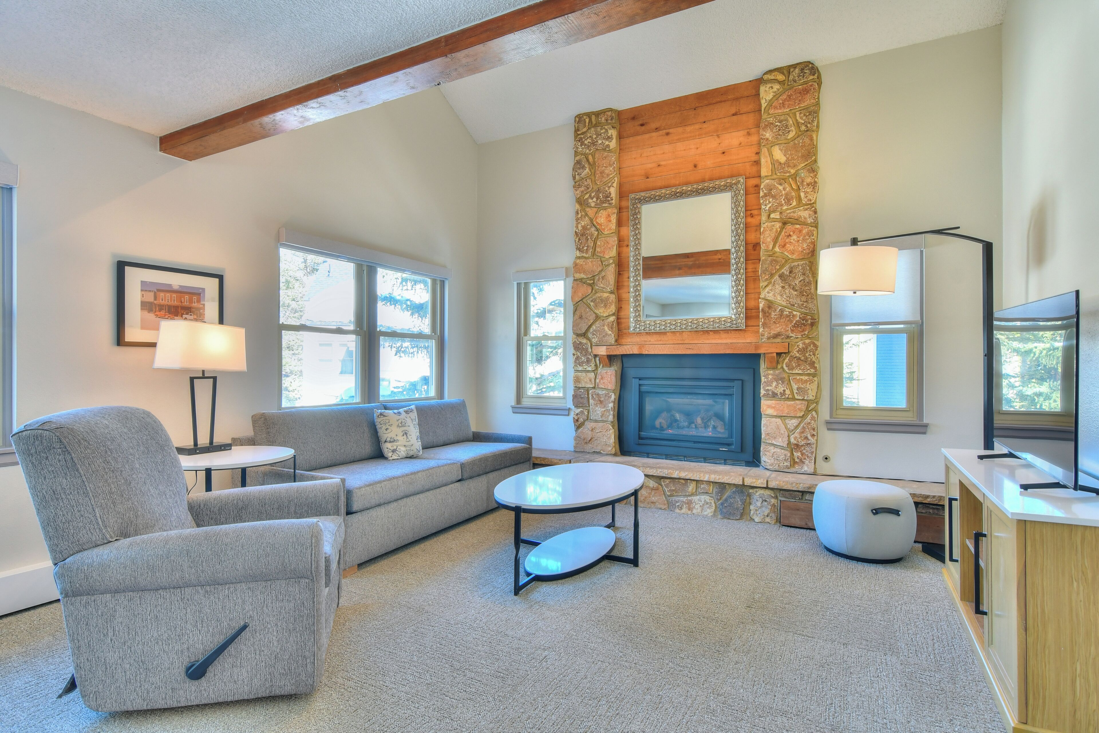 A living room with a stone fireplace, a sofa, a chair, a coffee table, and a TV stand.