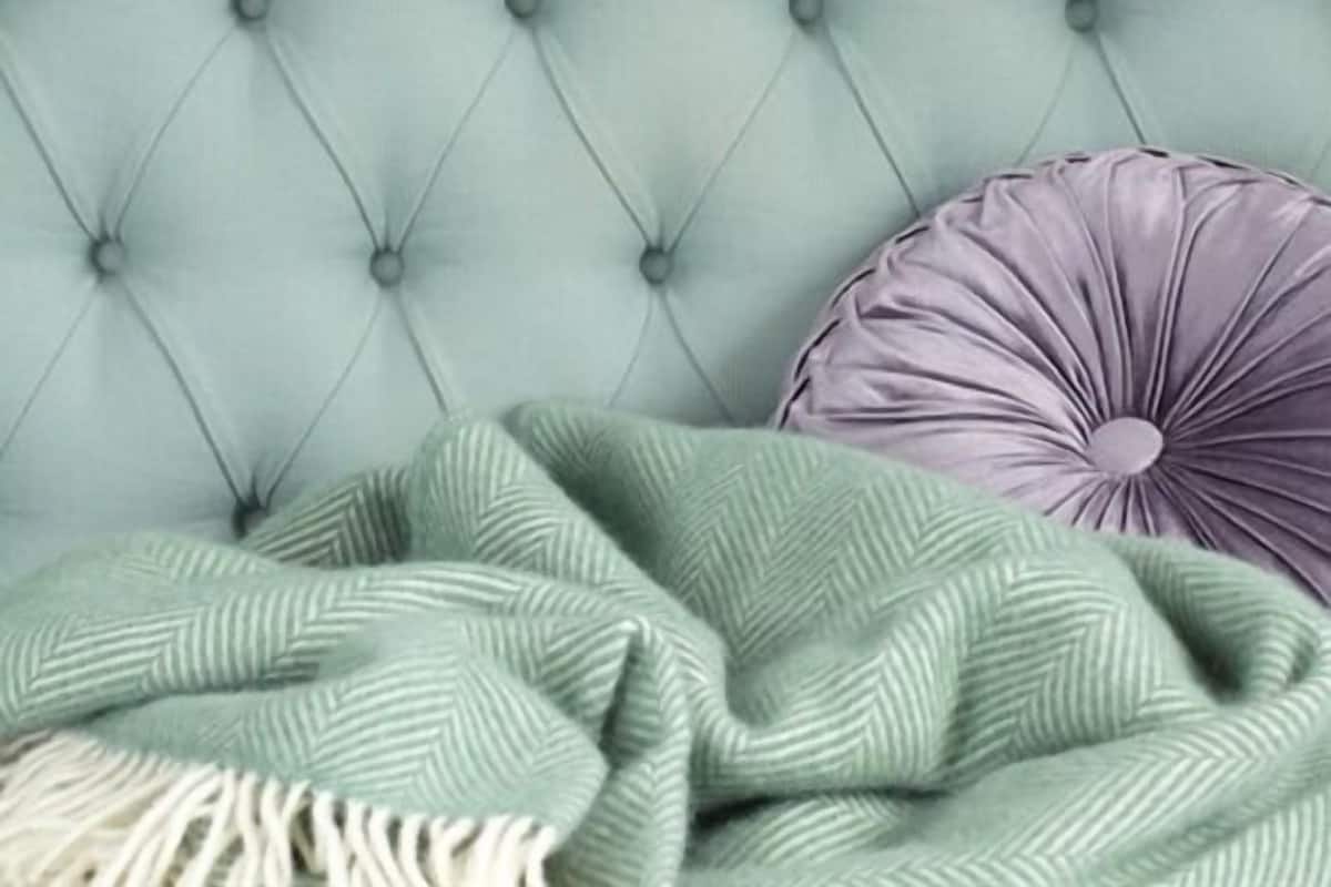 A tufted headboard with a herringbone-patterned throw blanket and a circular, ribbed pillow.