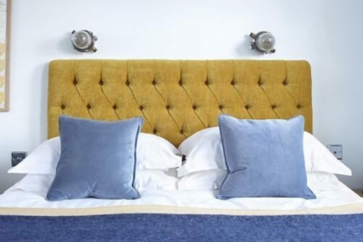 A bed with a tufted headboard, white bedding, and two blue pillows.