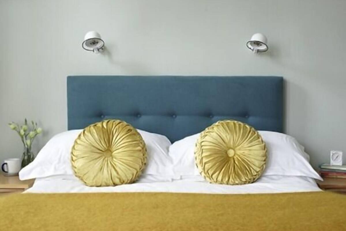 A bed with a blue headboard, two decorative pillows, white bedding, and two wall-mounted lamps.