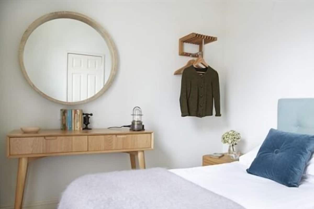 A bedroom with a bed, a bedside table, a dresser, a mirror, and a hanging garment organizer.